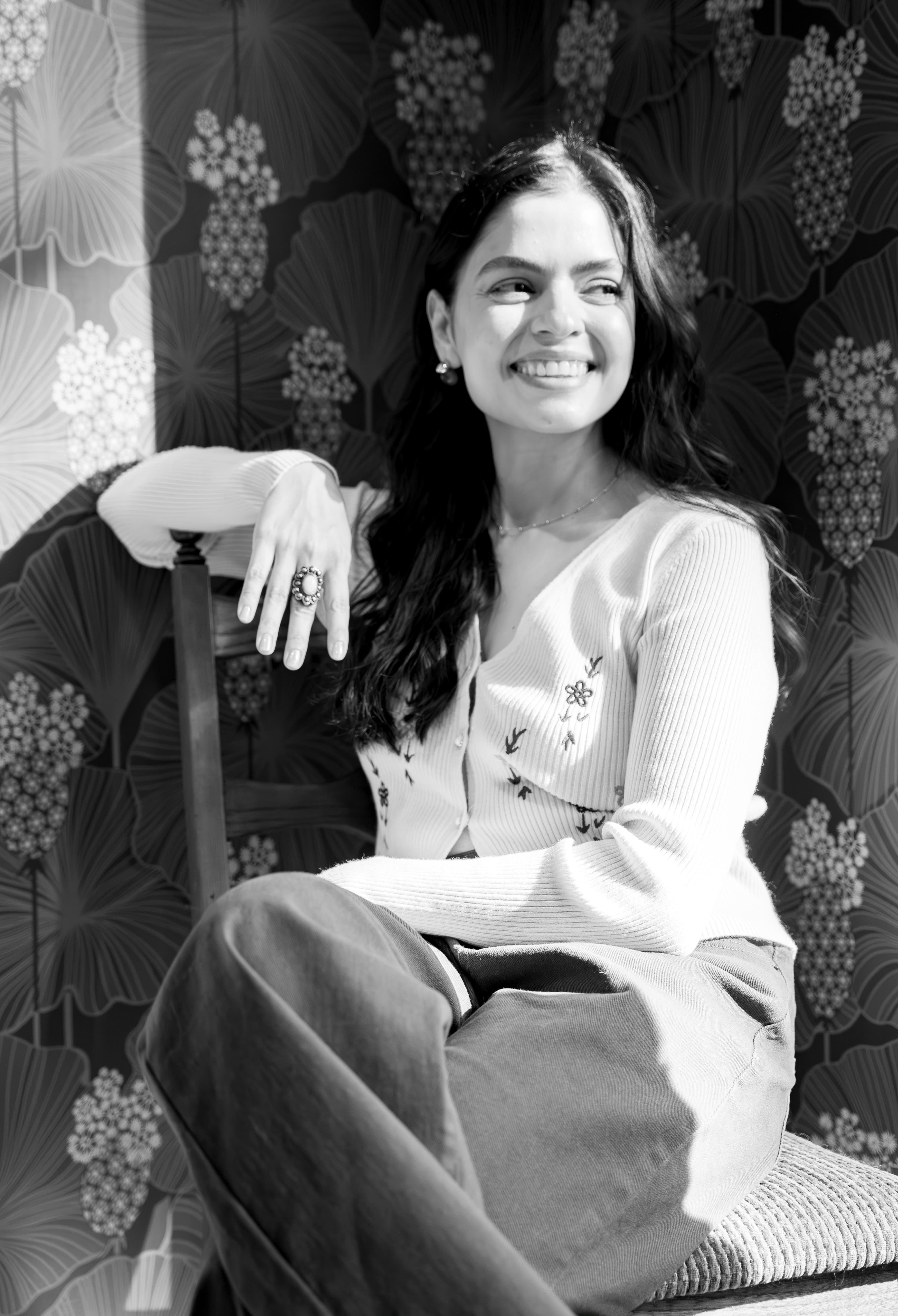Gabriela Herebia smiling, seated in front of a botanical patterned wall