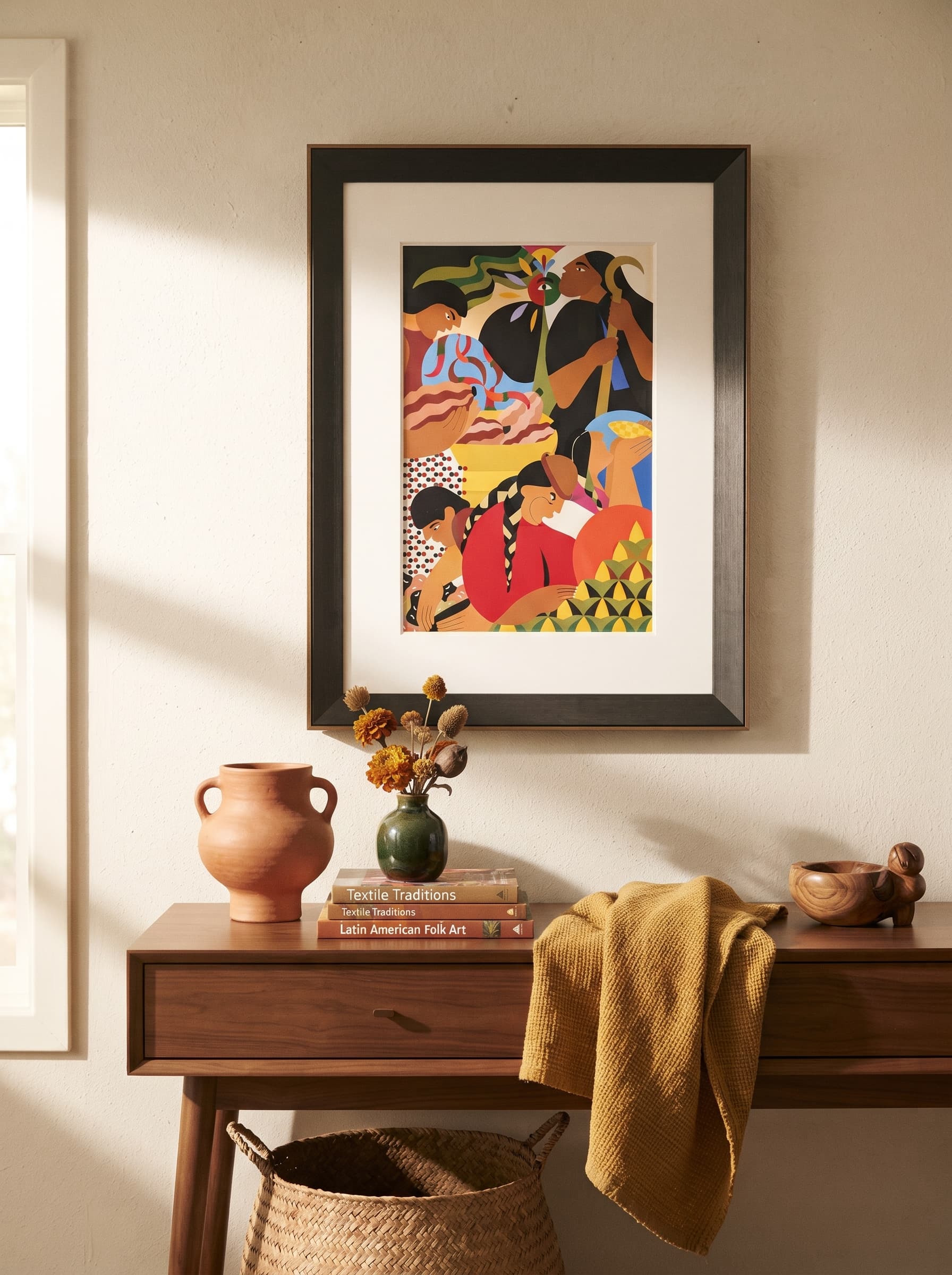 A framed Latin American folk-art print with a wide white mat on a warm plaster wall